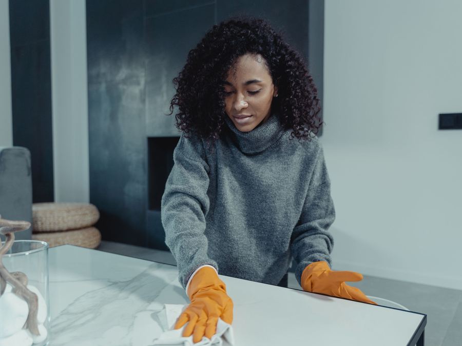 Cleaner in gloves wiping down a table in a bright, modern living room